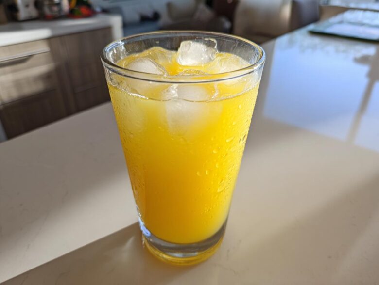 Close-up of a tall, sweating glass filled with bright yellow lemonade and ice cubes.
