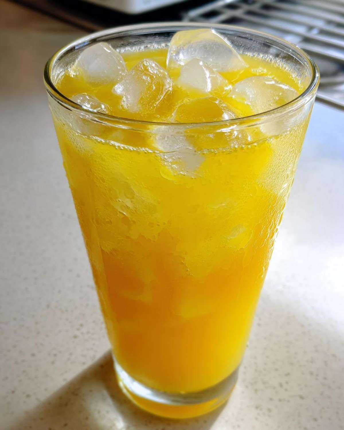 Close-up of a tall, sweating glass filled with bright yellow lemonade and plenty of ice cubes.