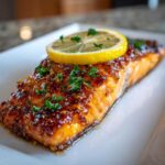 Close-up of a perfectly glazed baked salmon recipe fillet topped with a lemon slice and fresh parsley.