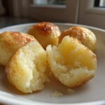 Close-up of fluffy, golden-brown potato dumplings, one split open to show the soft interior.