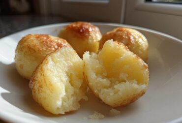 Close-up of fluffy, golden-brown potato dumplings, one split open to show the soft interior.