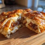 A golden brown, flaky pastry wrapped baked brie, cut open to show the melted cheese and caramelized topping.