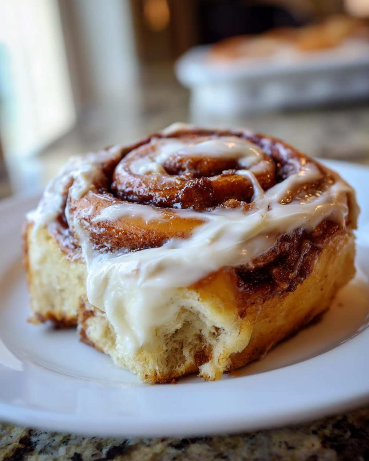 Close-up of a fluffy, gooey cinnamon buns with thick white cream cheese frosting, showing a bite taken out.