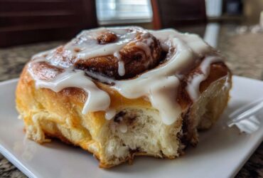 A close-up of a fluffy, freshly baked cinnamon bun generously topped with thick white icing.