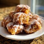 A stack of freshly made, gooey cinnamon roll bites drizzled generously with white icing on a white plate.