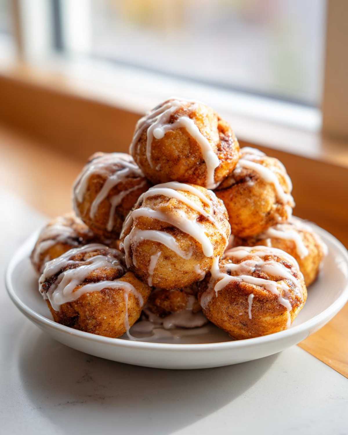 A stack of freshly made cinnamon roll bites drizzled generously with white icing, served on a white plate.