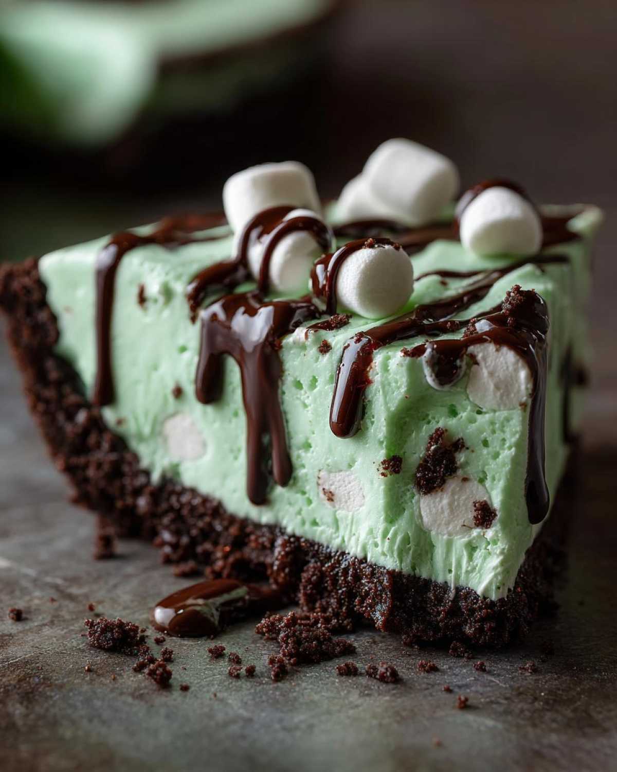 A decadent slice of bright green grasshopper pie with a dark chocolate crust, topped with chocolate syrup and mini marshmallows.