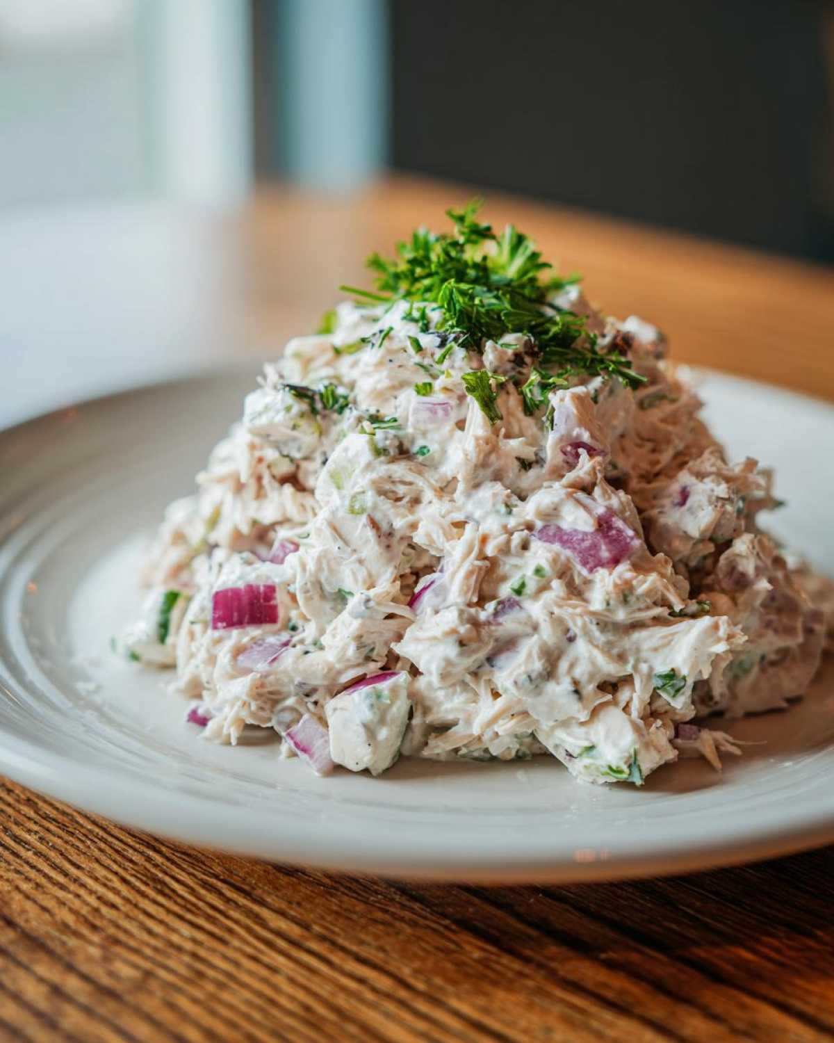 A close-up of a generous serving of greek yogurt chicken salad, mixed with red onion and topped with fresh parsley.