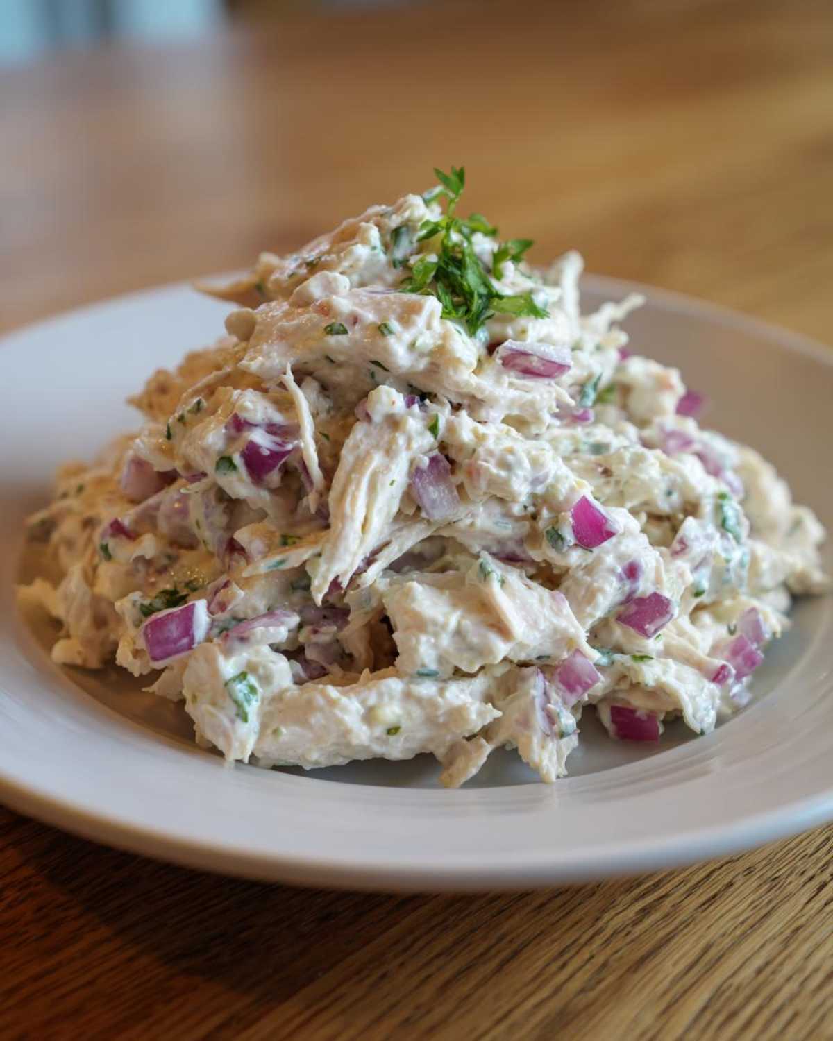 A close-up of a generous serving of greek yogurt chicken salad mixed with red onion, topped with fresh parsley.