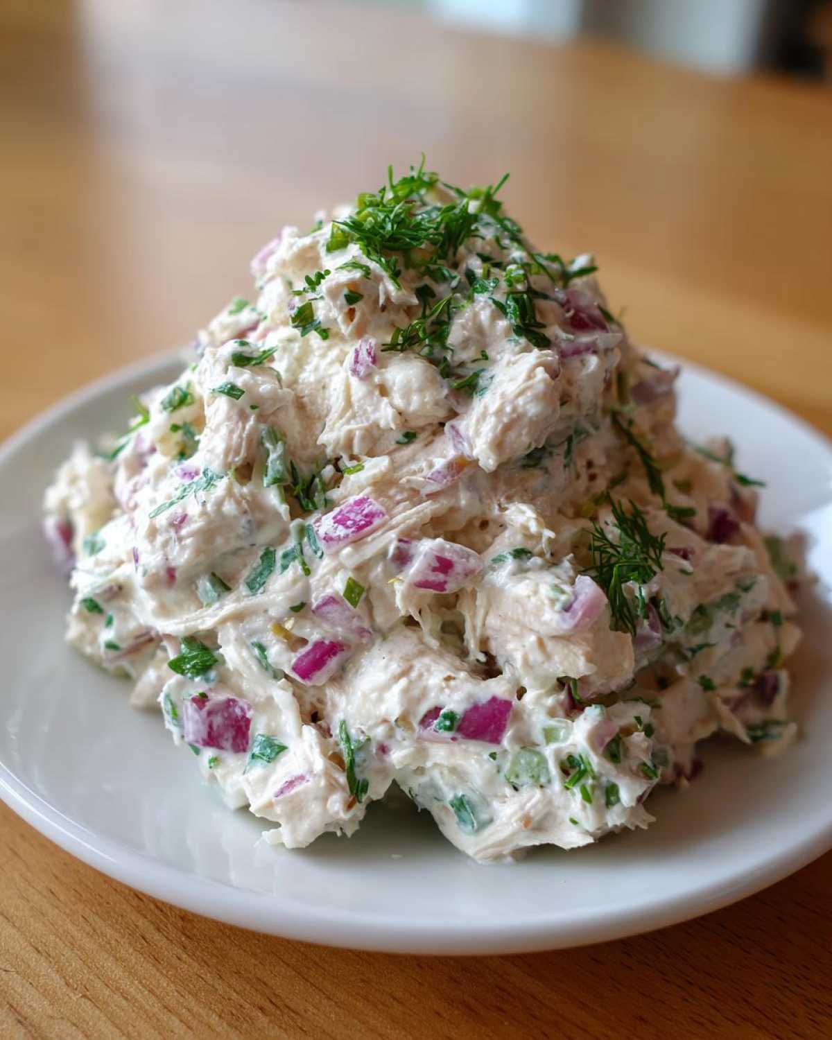 A generous serving of creamy greek yogurt chicken salad mixed with diced red onion and fresh herbs, piled high on a white plate.