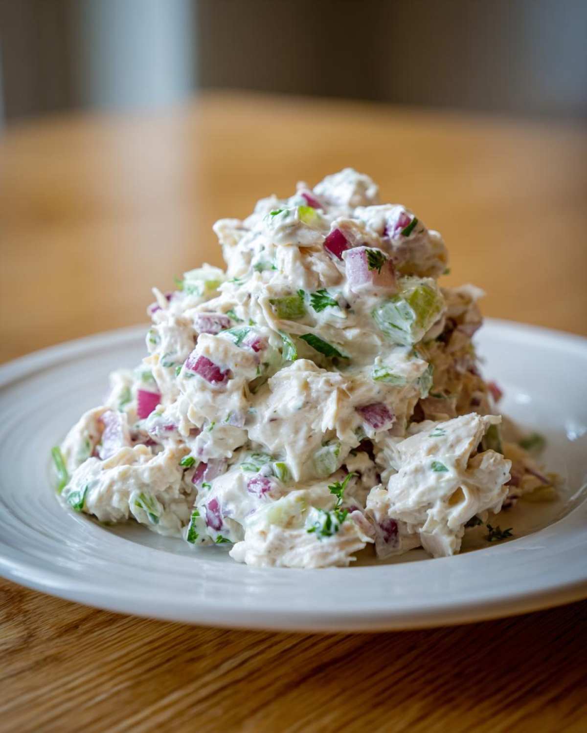 A mound of creamy greek yogurt chicken salad mixed with visible chunks of red onion and celery on a white plate.