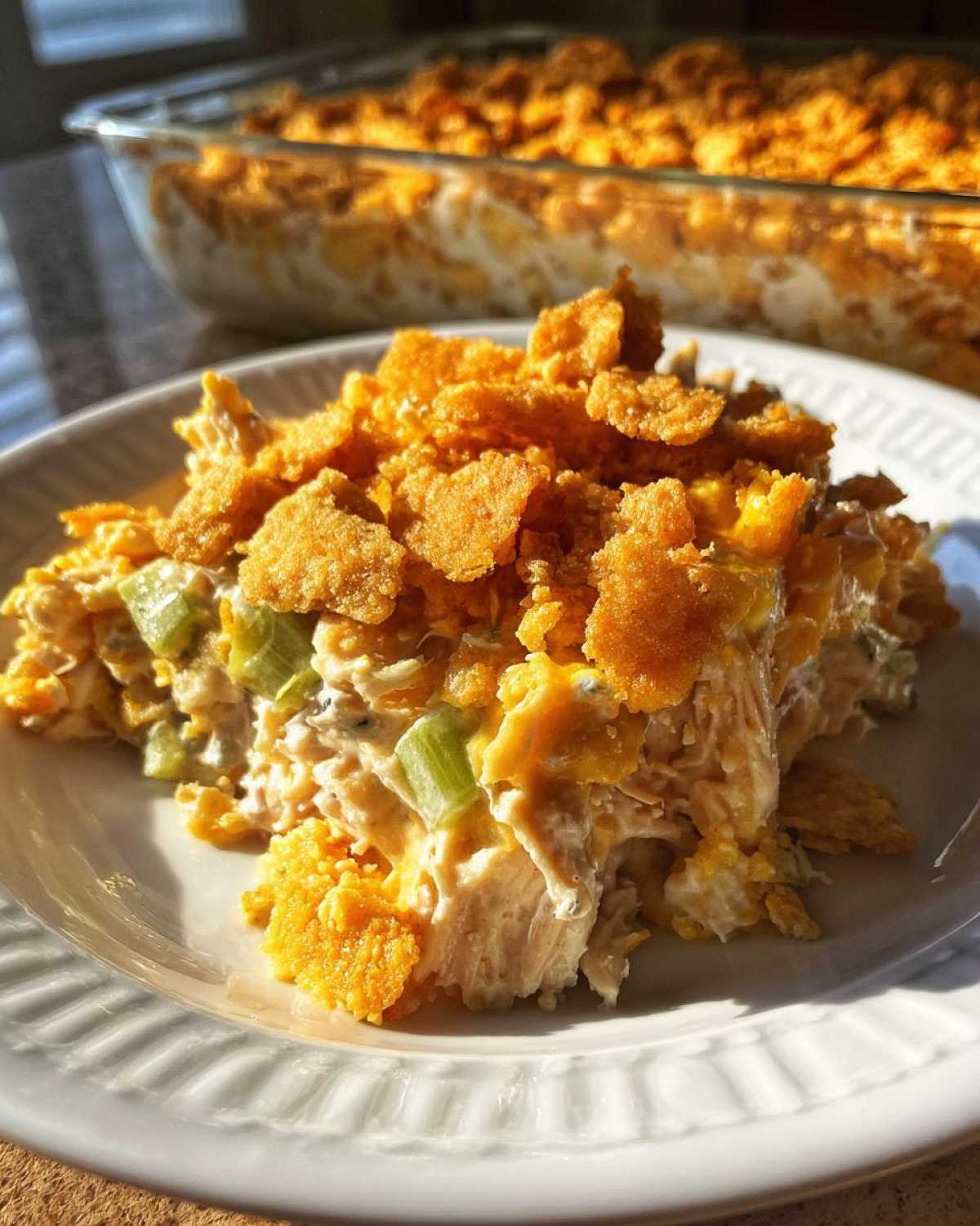 A serving of creamy hot chicken salad mixed with celery and topped with crunchy, golden cornflakes on a white plate.