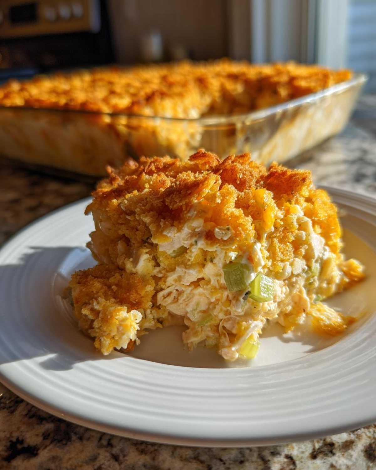 A serving of creamy hot chicken salad topped with a golden, crunchy crust, served on a white plate.