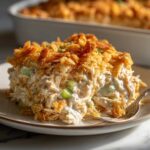 A close-up serving of creamy hot chicken salad topped with a thick layer of crispy, golden crushed crackers or chips.