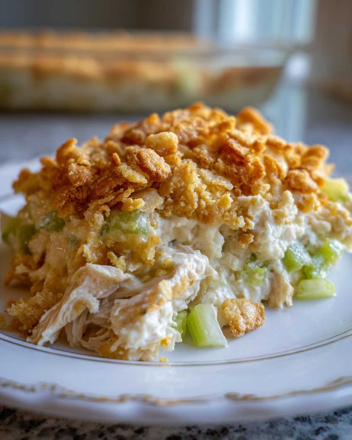 A close-up serving of creamy hot chicken salad topped with a golden, crunchy cornflake crust.