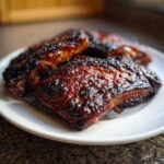 Close-up of several juicy, caramelized pork steak recipe portions with a dark, sticky glaze served on a white plate.