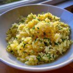 Close-up of fluffy, yellow Mediterranean rice garnished with fresh green herbs in a white bowl.
