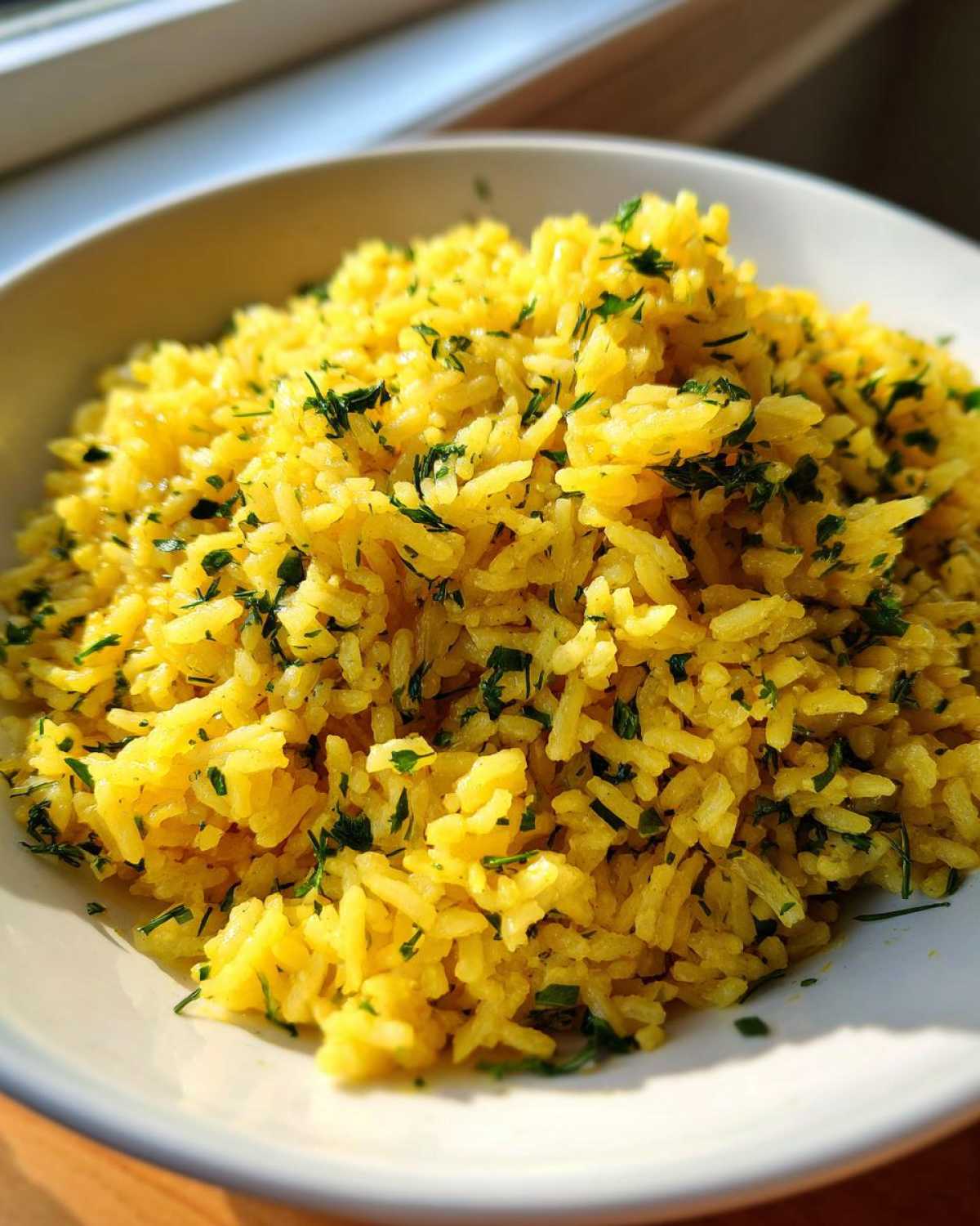 Close-up of fluffy, yellow mediterranean rice garnished generously with chopped green herbs.