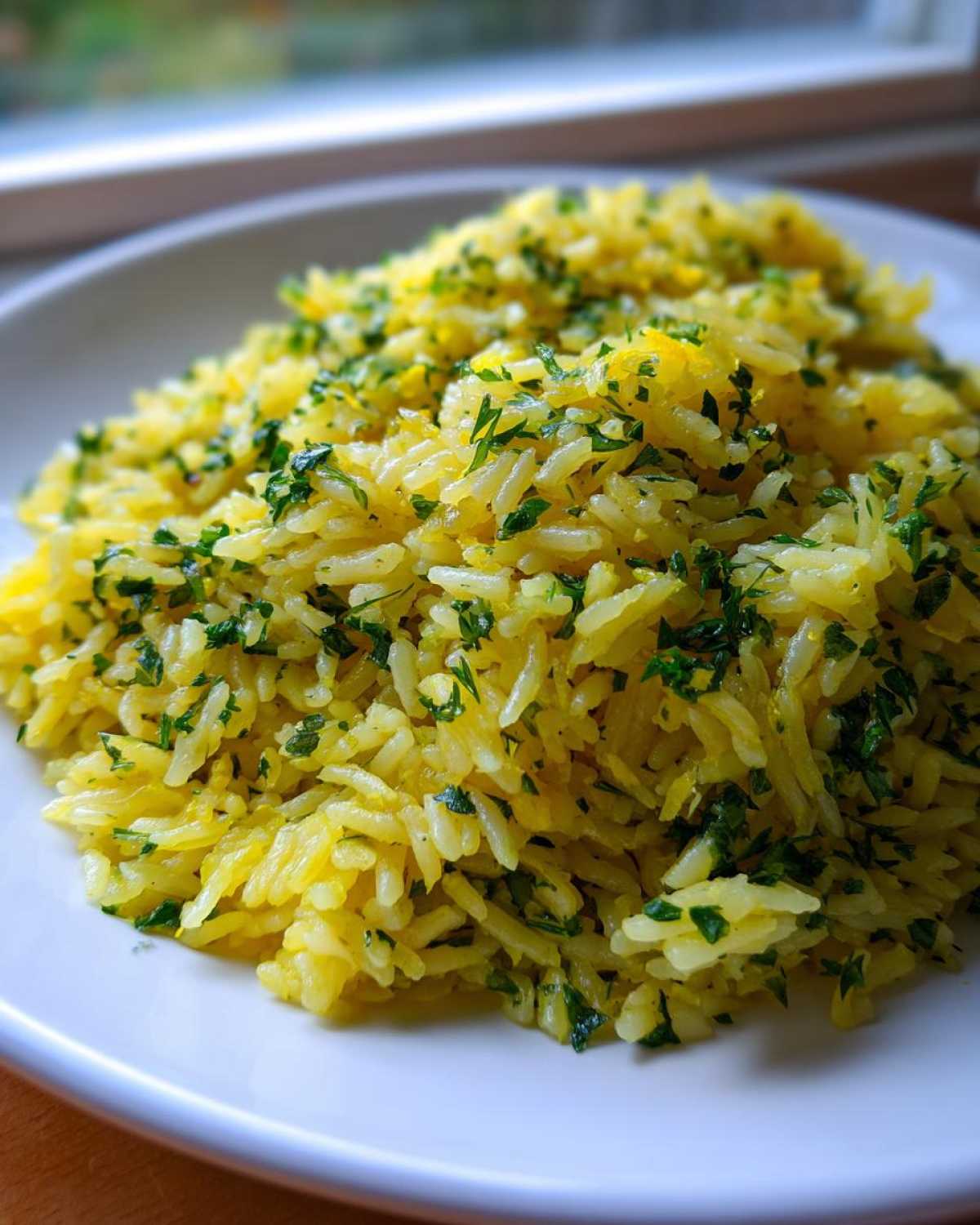 Close-up of fluffy, yellow-tinted mediterranean rice topped generously with fresh chopped parsley on a white plate.