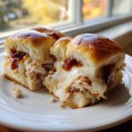 Close-up of two delicious bbq chicken sliders filled with shredded meat, melted white cheese, and BBQ sauce on a white plate.