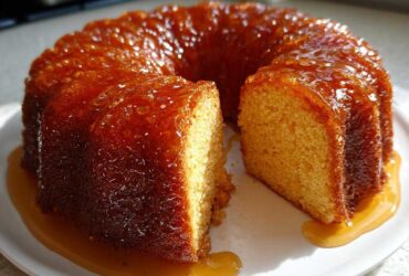 A moist Bacardi Rum Cake, glazed with a shiny caramel sauce, with one slice cut out on a white plate.