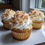 Three moist coconut cupcakes topped with white frosting and generous flakes of toasted coconut.
