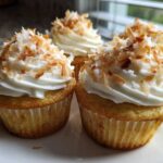 Close-up of moist coconut cupcakes topped with white frosting and toasted coconut flakes.