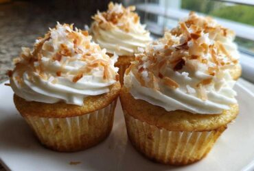 Close-up of moist coconut cupcakes topped with white frosting and toasted coconut flakes.