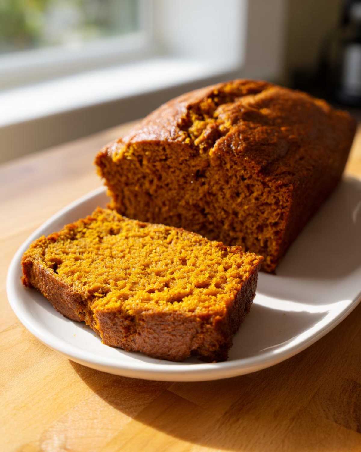 A moist pumpkin bread loaf with one slice cut and resting on a white plate.