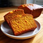 Two moist slices of rich orange pumpkin bread served on a white plate with the loaf in the background.
