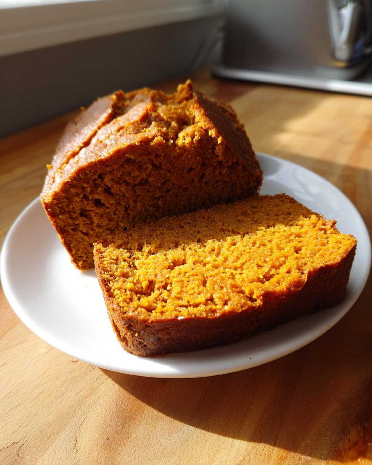 A loaf of moist pumpkin bread with one slice cut and resting on a white plate.