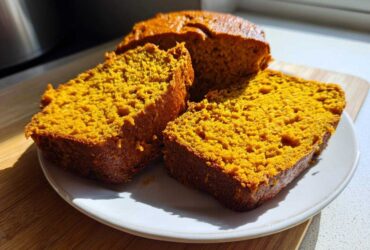 Close-up of three thick, moist slices of bright orange pumpkin bread on a white plate.