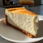 A thick, creamy slice of new york cheesecake with a graham cracker crust, perfectly golden brown on top.