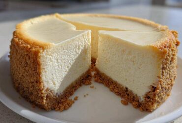 A whole, crack-free new york cheesecake with two slices cut out, showing a thick graham cracker crust.