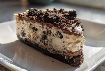 A close-up of a rich slice of no bake Oreo pie showing the creamy filling with cookie chunks and a dark chocolate crust.