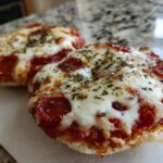 Two freshly baked pepperoni pizza bagels topped with melted mozzarella cheese and dried herbs, ready to eat.