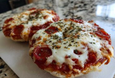 Two freshly baked pepperoni pizza bagels topped with melted mozzarella cheese and dried herbs, ready to eat.