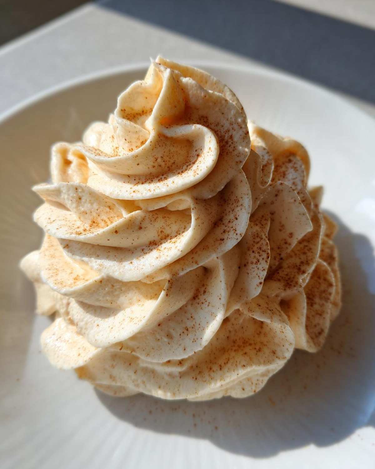 Close-up of a beautifully piped swirl of light brown cinnamon butter, dusted with ground cinnamon.