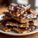 Close-up of a stack of broken pieces of rich saltine cracker toffee topped with shiny dark chocolate.