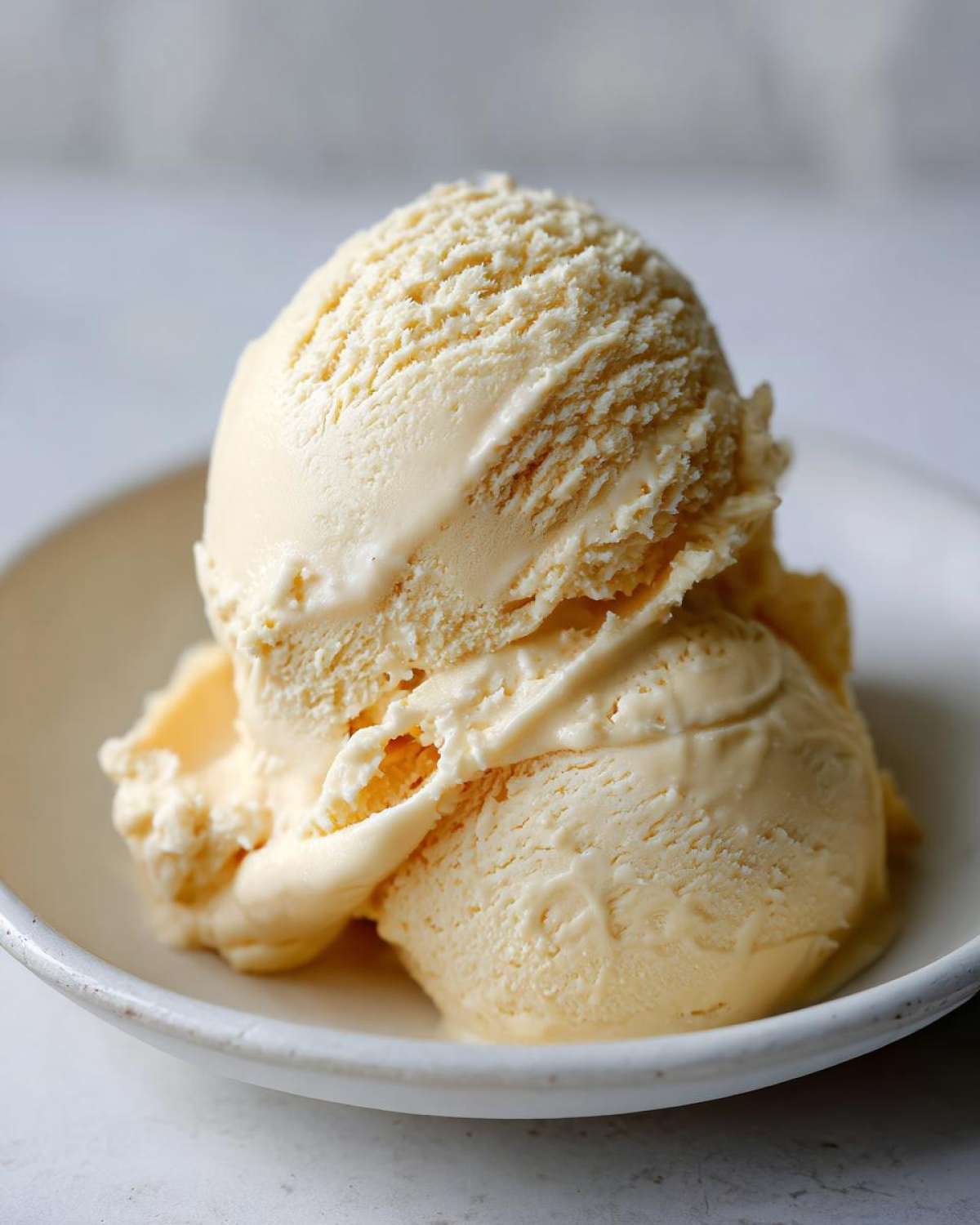 Two scoops of creamy, pale yellow banana ice cream served in a small white bowl.