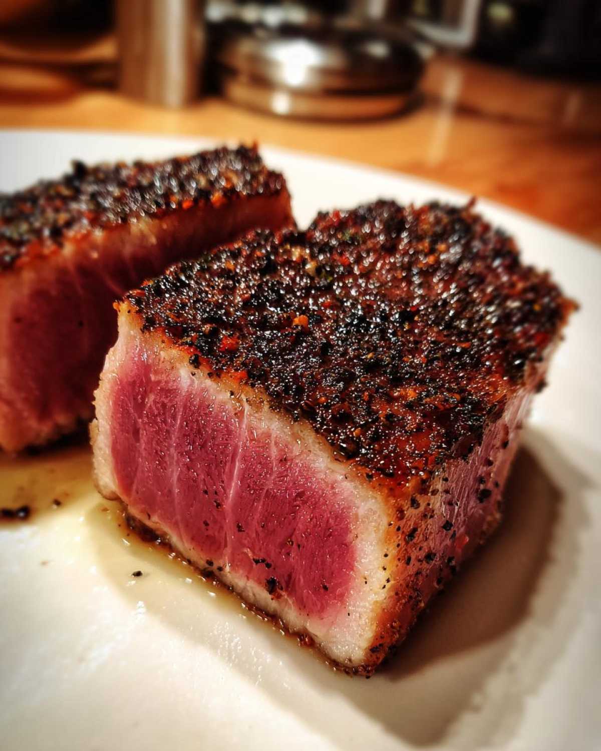 Close-up of two perfectly seared Tuna Steaks, showing a deep red, rare center and a heavily peppered crust.