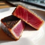 Two cross-sections of perfectly seared tuna steaks showing a deep red, rare center and a dark, seasoned crust.