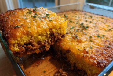 A slice being lifted from a baked tamale pie, showing layers of seasoned ground beef and a thick, cheesy cornbread topping.