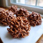 A close-up of several glossy, chocolate-coated haystack cookies resting on a white platter.