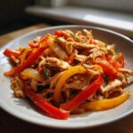 Close-up of shredded chicken mixed with sliced red and yellow bell peppers and onions, ready for crockpot chicken fajitas.