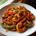 Close-up of seasoned shrimp fajitas with sautéed red and green bell peppers and onions on a white plate.