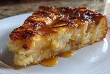 Close-up of a rich, gooey slice of caramel apple dump cake drizzled with caramel sauce.
