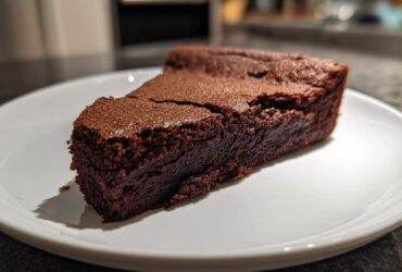A dense, dark slice of flourless chocolate cake resting on a white plate, showing its fudgy texture.