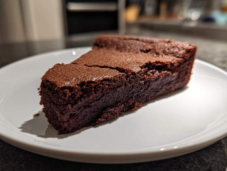 A dense, dark slice of flourless chocolate cake resting on a white plate, showing its fudgy texture.