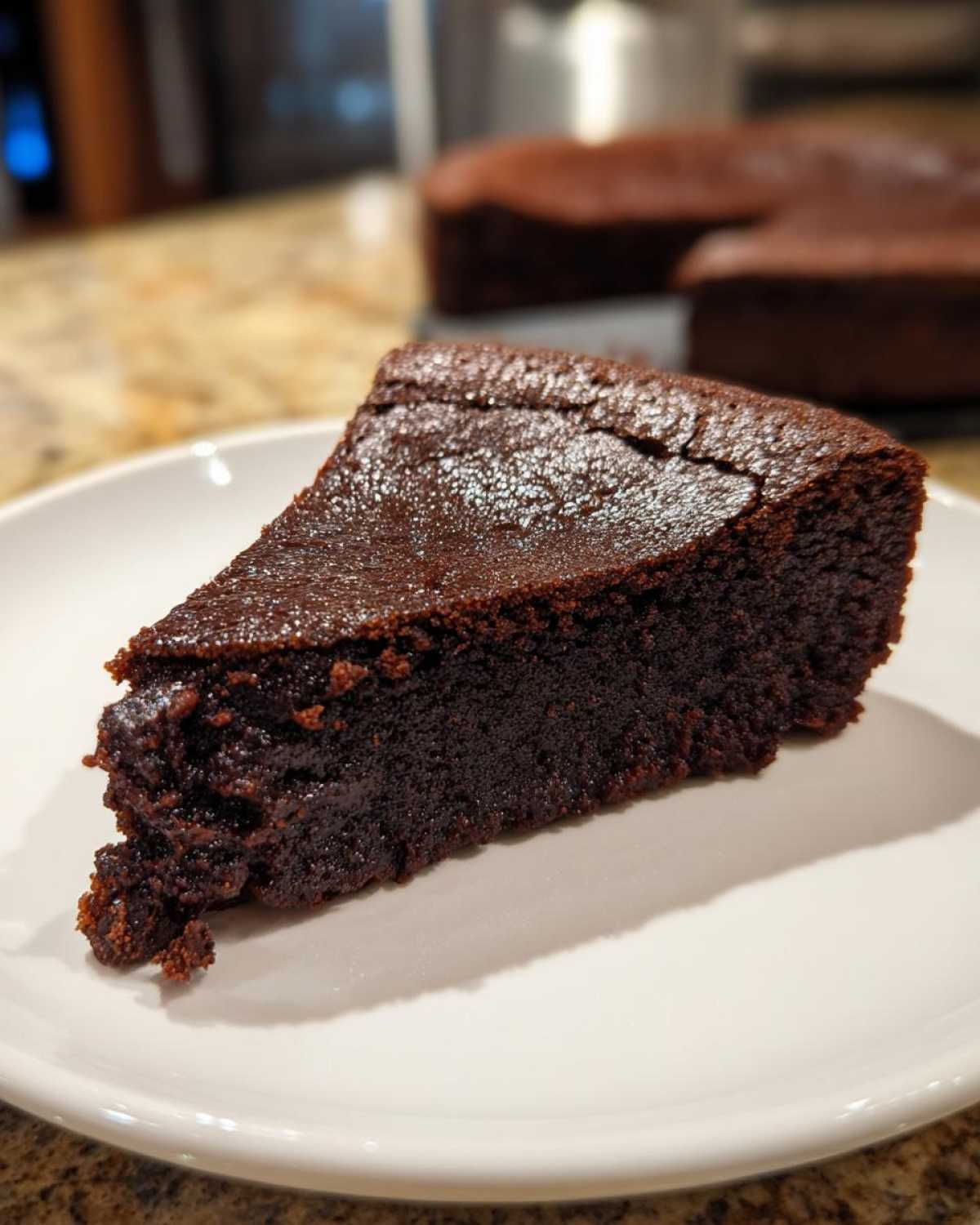 A close-up of a dense, dark slice of flourless chocolate cake served on a white plate.